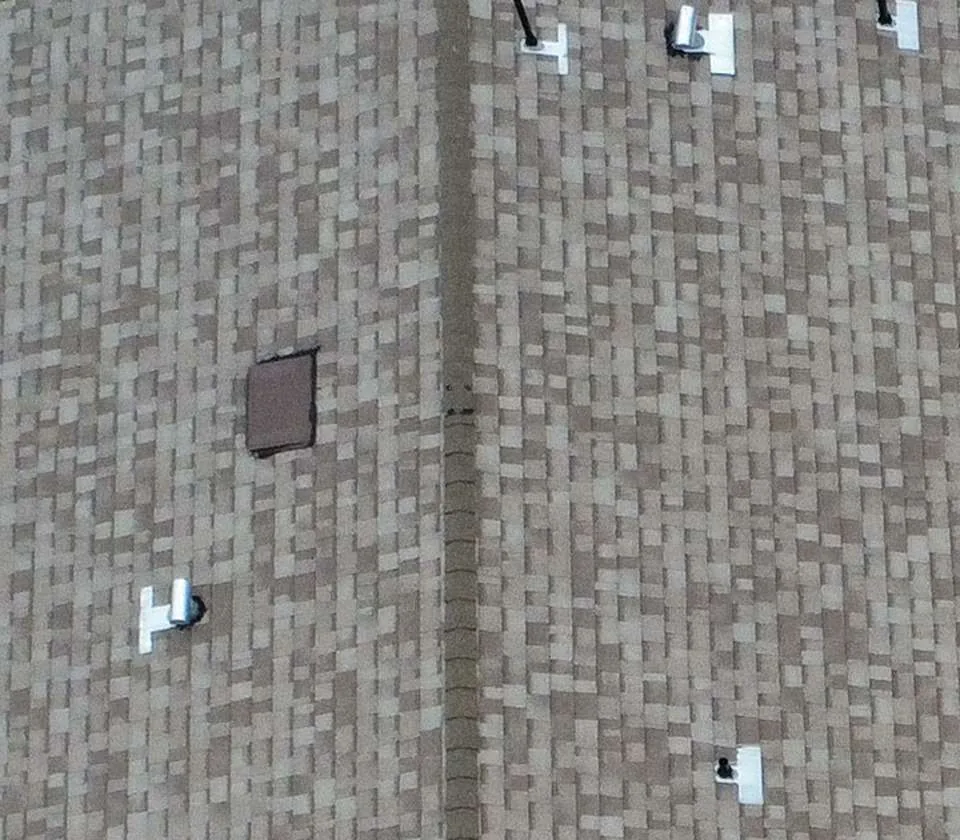 Overhead view of a gray-brown asphalt shingle roof with several small penetrations and a center ridge
