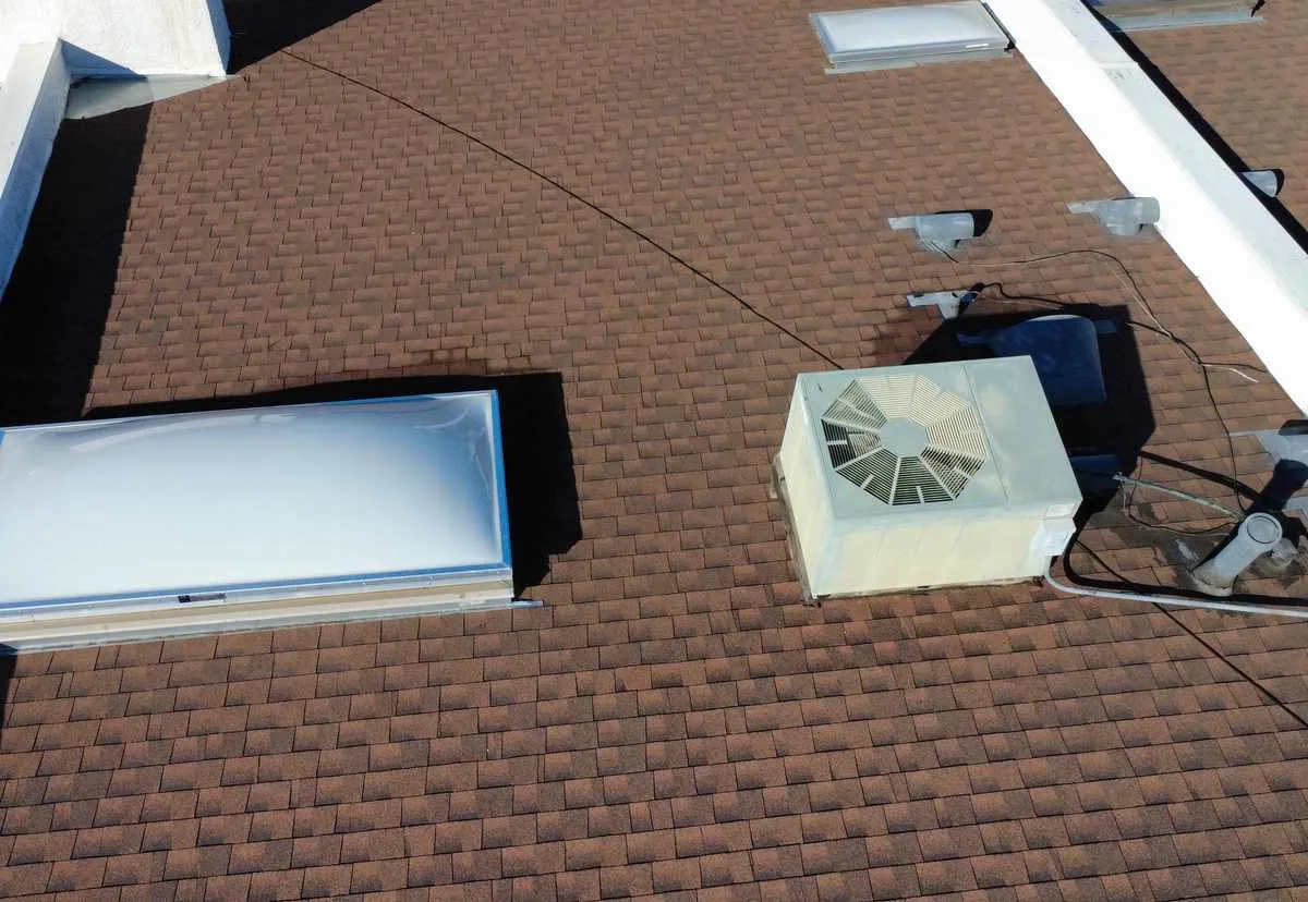 Brown asphalt shingle roof seen from above with two skylights, a rooftop HVAC unit, vent pipes and surface cabling