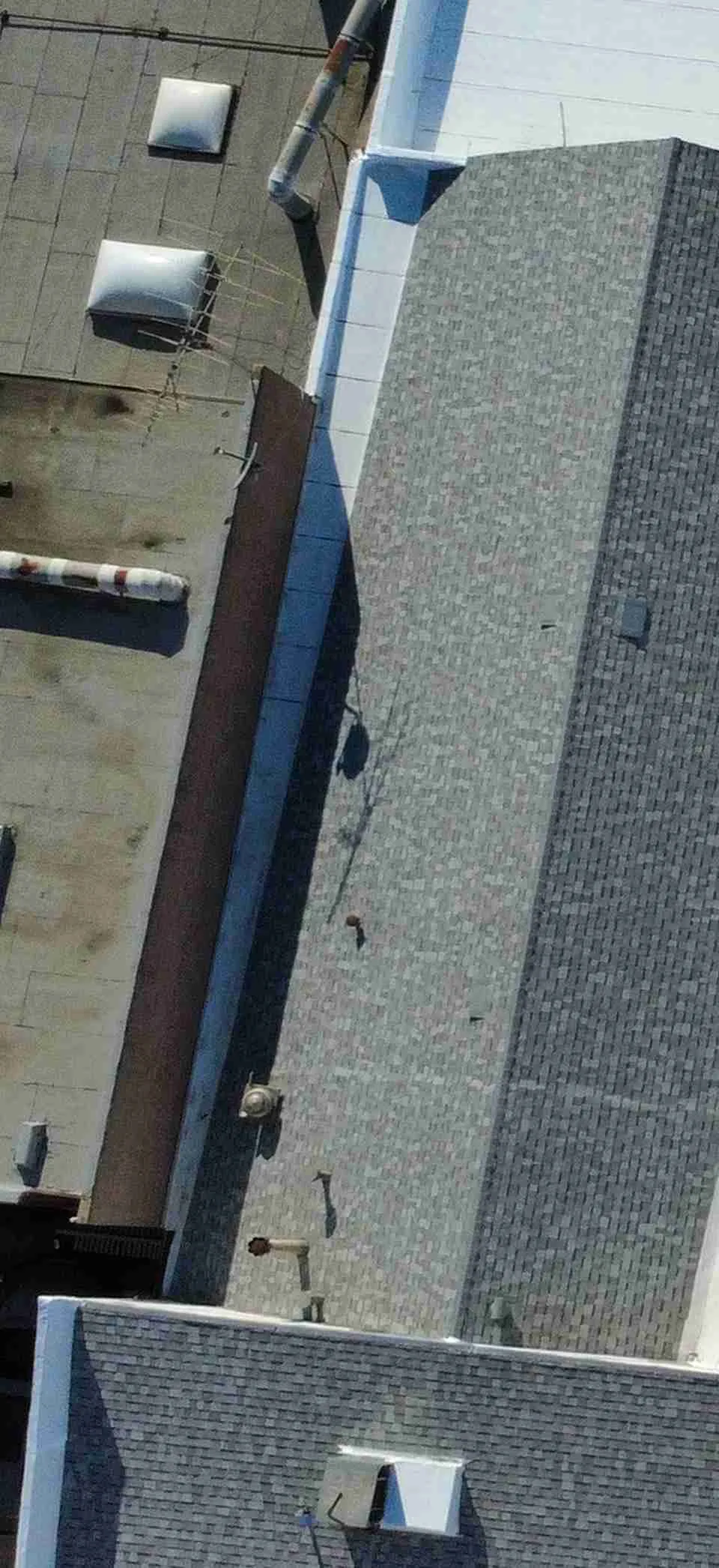 Aerial view of adjoining white low-slope roof planes and gray shingle sections, with rooftop equipment and solar panels on nearby roof areas.