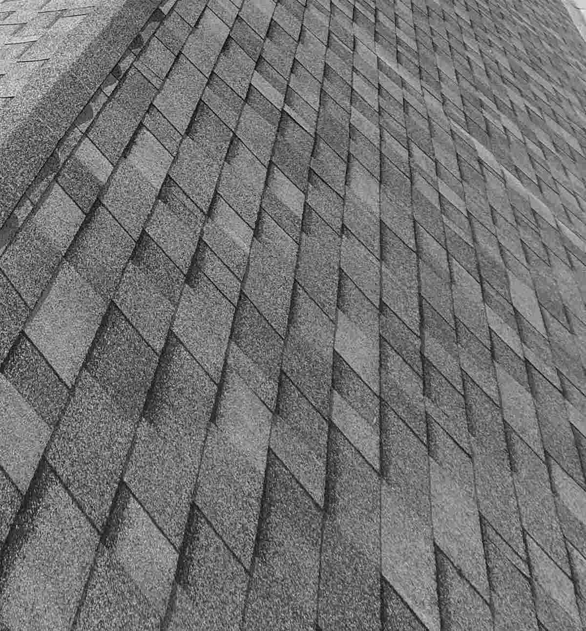 Elevated view along a gray asphalt shingle ridge and the roof planes beside it under a bright sky