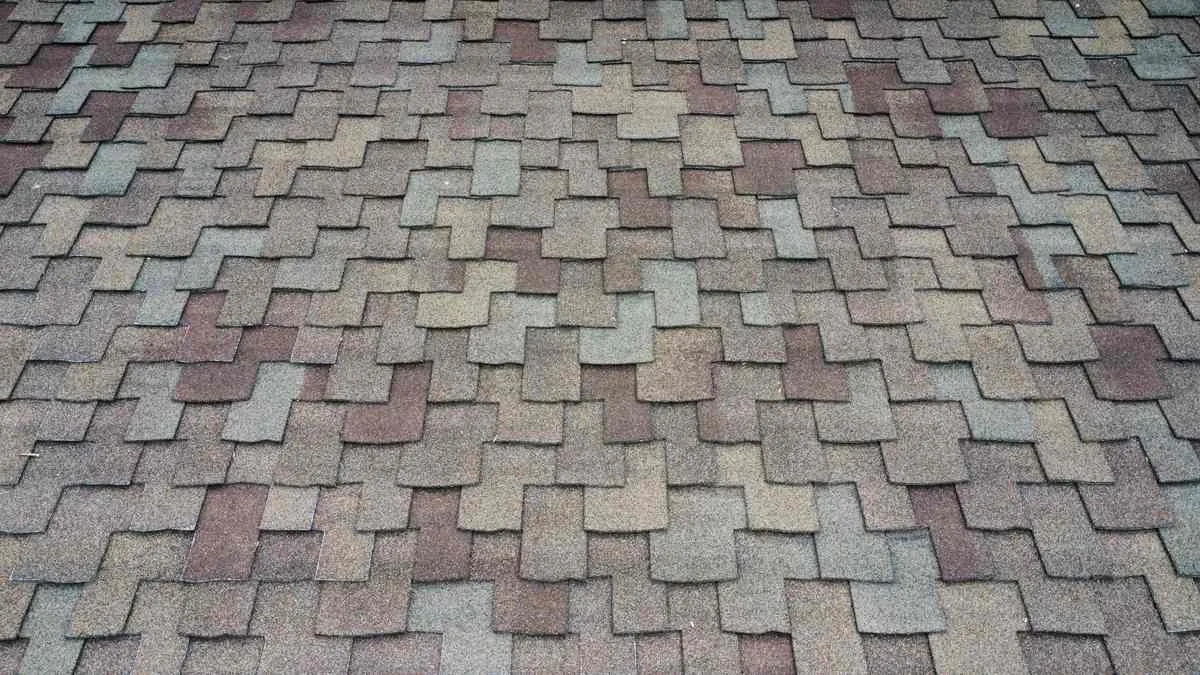 Close view of multitone asphalt shingles with gray, tan, muted red, and greenish granule patches