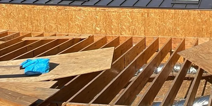 Dark standing-seam metal panels above open wood roof-deck framing with rectangular openings
